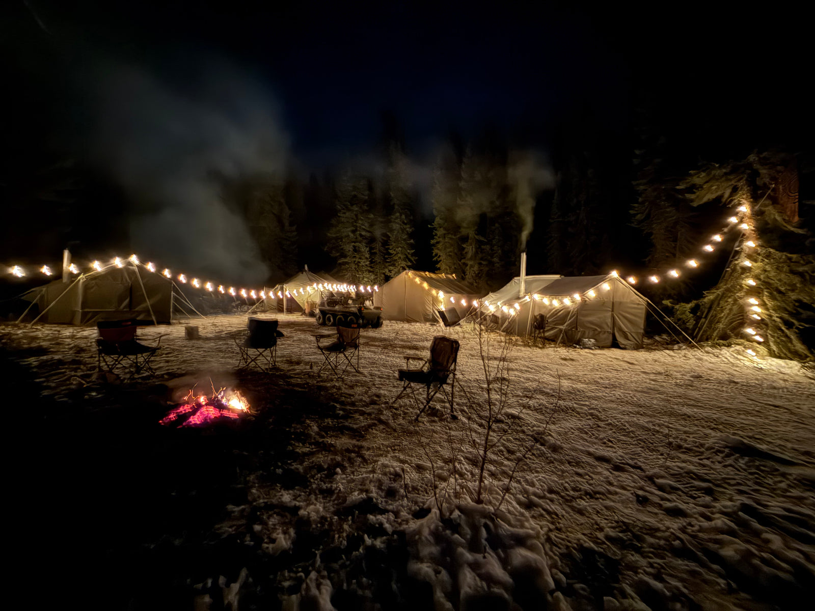 Camp at night with strung lights and a fire burning