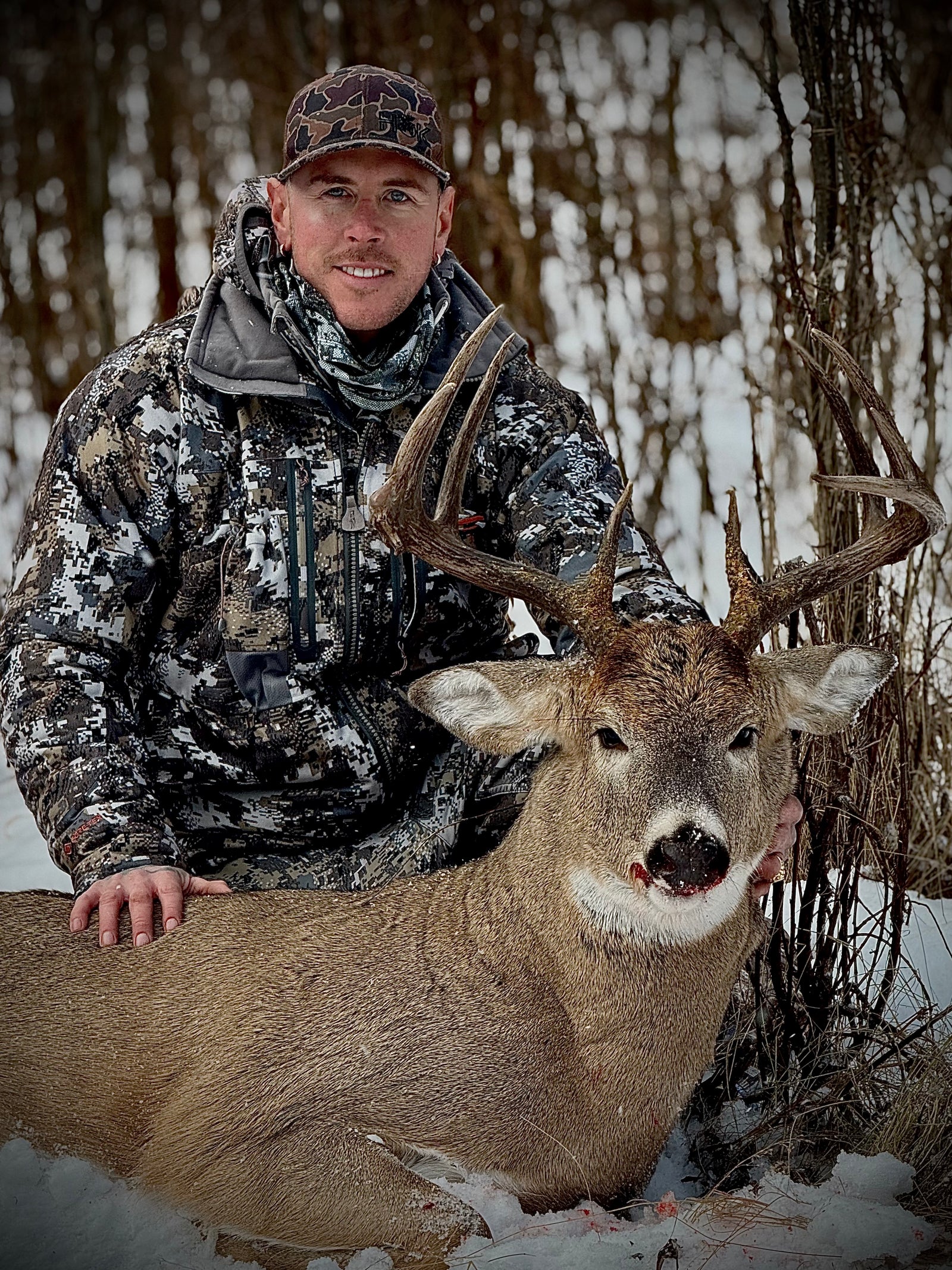 Hunter with a heavy-racked whitetail buck in the snow