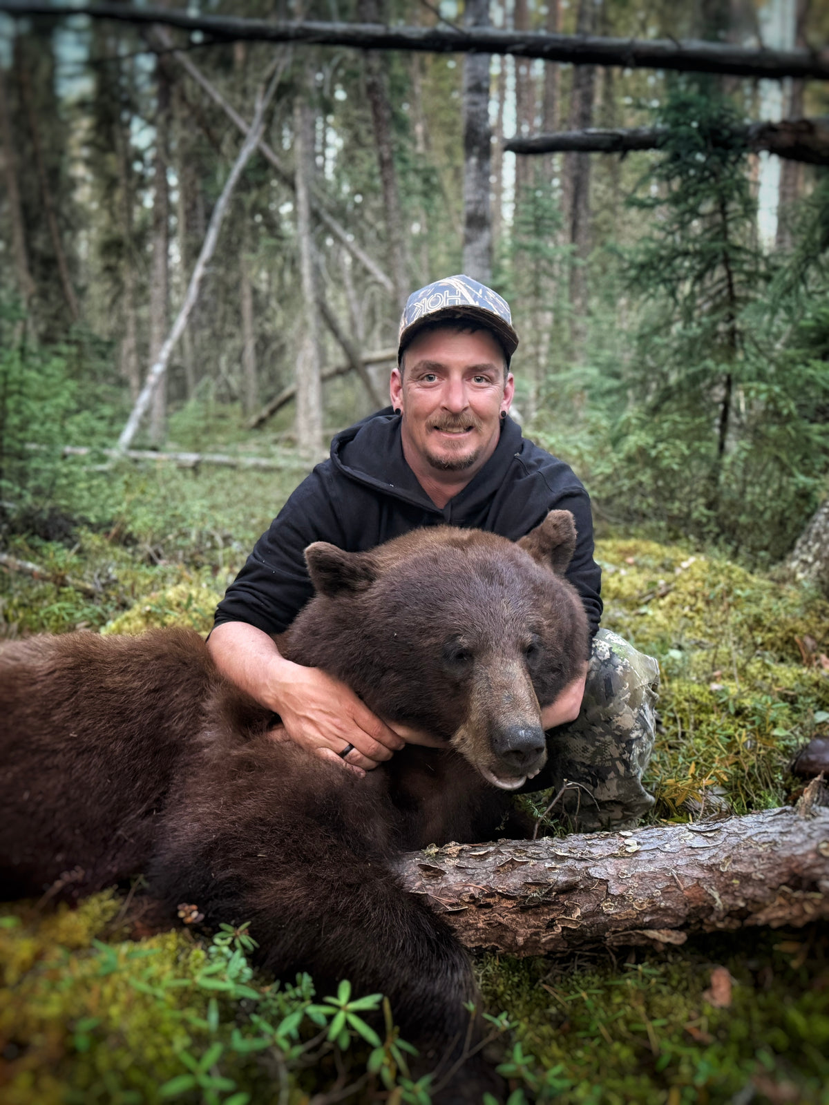 Hunter with a black bear on a mossy forest floor